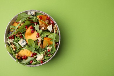Tasty salad with persimmon, blue cheese, pomegranate and walnuts served on light green background, top view. Space for text