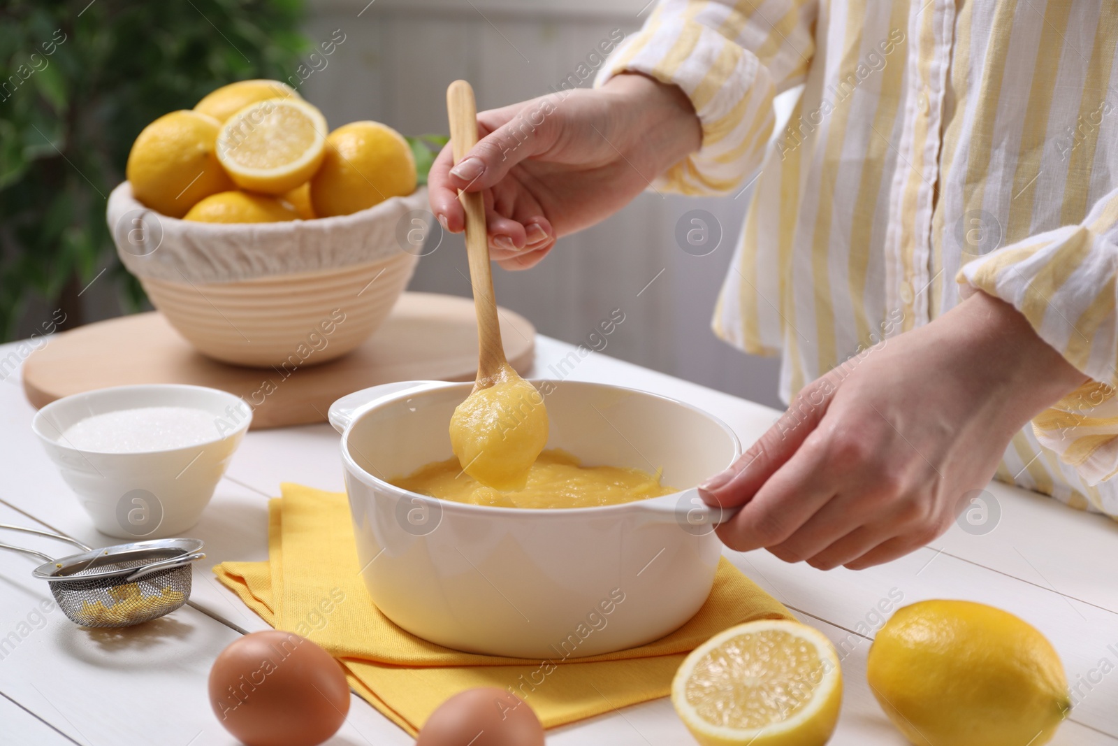 Photo of Woman cooking lemon curd at white wooden table, closeup