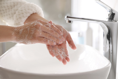 Woman washing hands with soap over sink in bathroom, closeup