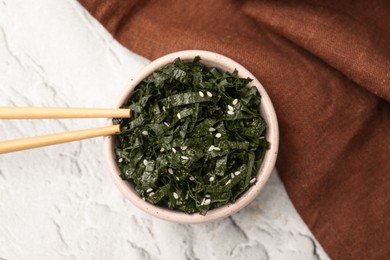 Chopped nori sheets with sesame and chopsticks on white textured table, flat lay