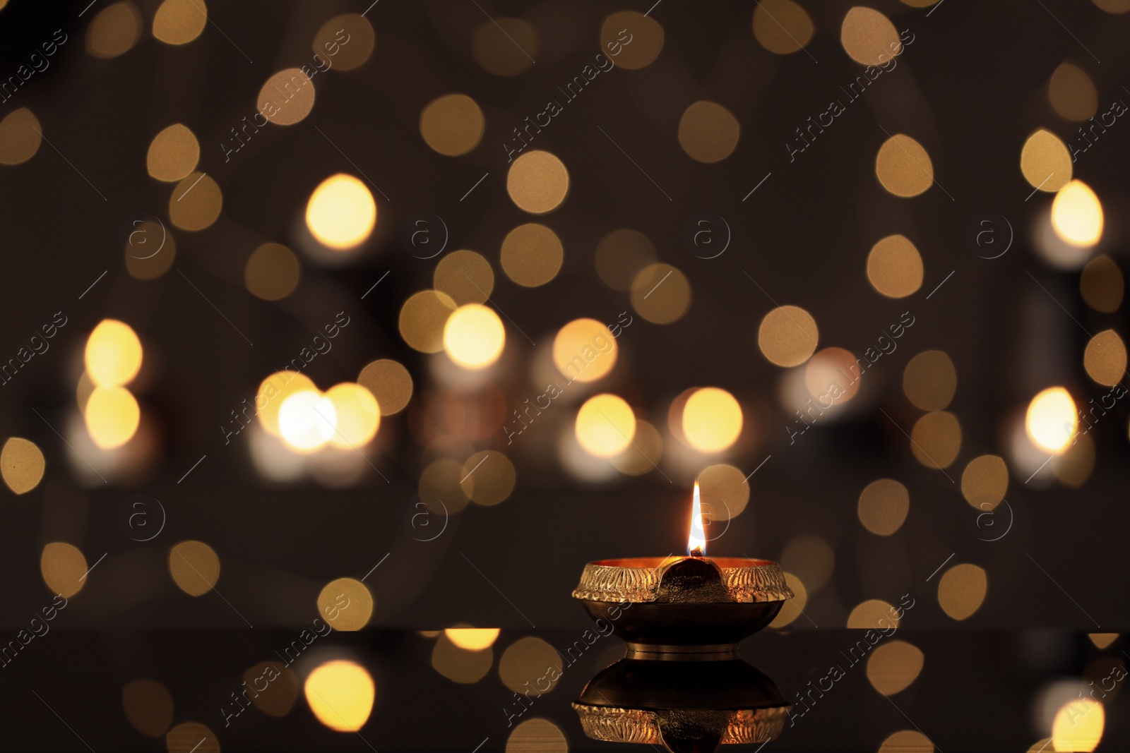 Photo of Lit diya on table against blurred lights, space for text. Diwali lamp