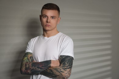 Photo of Young man with tattoos near light wall. Space for text