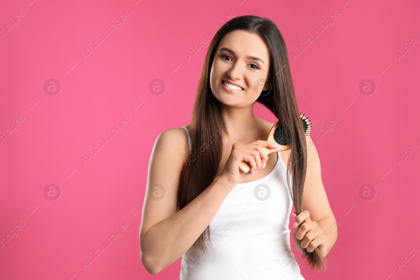 Photo of Beautiful smiling young woman with hair brush on color background