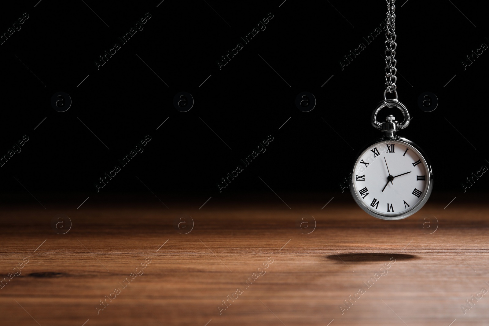 Photo of Beautiful vintage pocket watch with silver chain on black background above wooden table, space for text. Hypnosis session