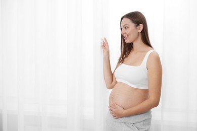 Beautiful pregnant woman near window indoors, space for text