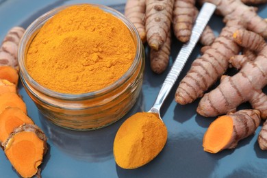 Photo of Glass jar of turmeric powder and roots on plate, closeup