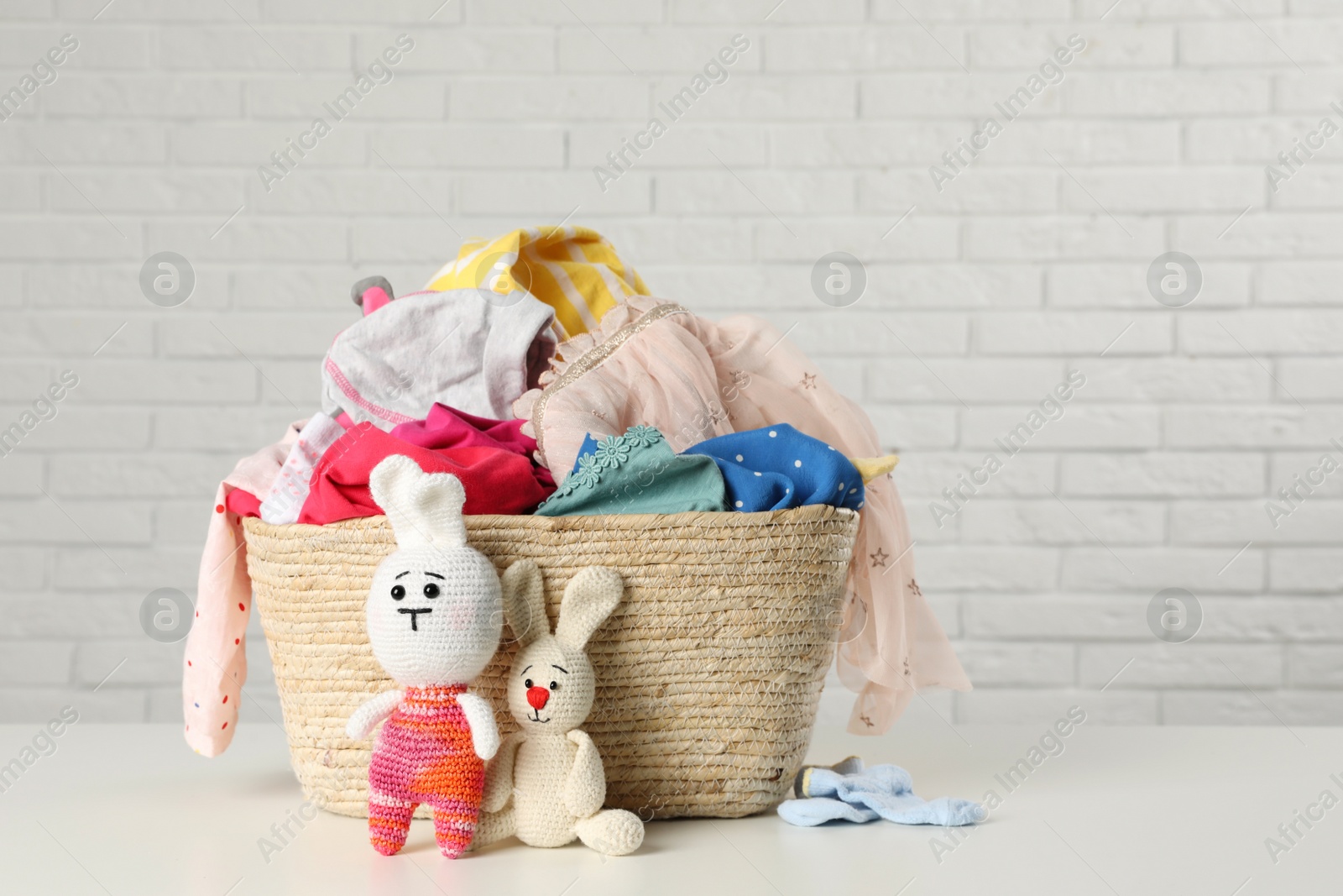 Photo of Wicker basket with laundry and toys on table near white brick wall