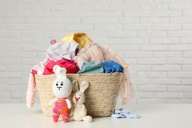 Photo of Wicker basket with laundry and toys on table near white brick wall