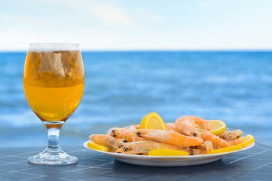 Photo of Cold beer in glass and shrimps served with lemon on beach