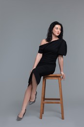 Photo of Beautiful woman in dress on stool against grey background