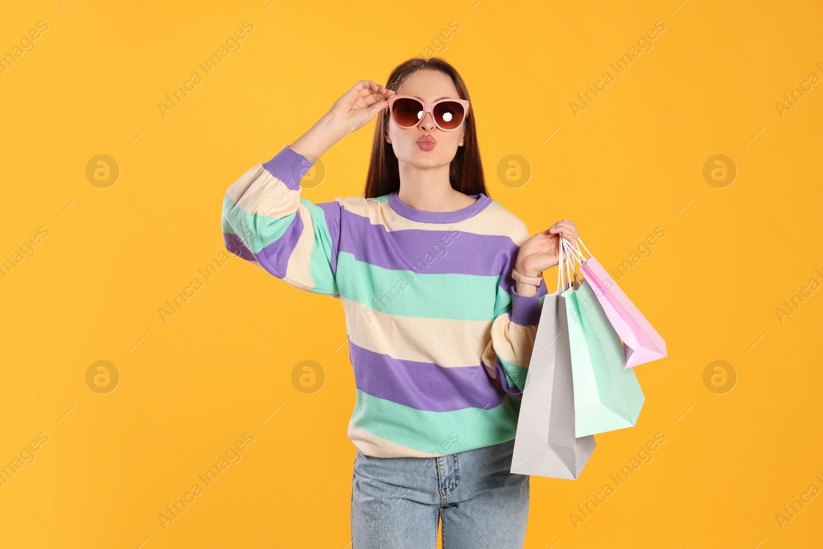 Photo of Beautiful young woman with shopping bags on yellow background. Big sale