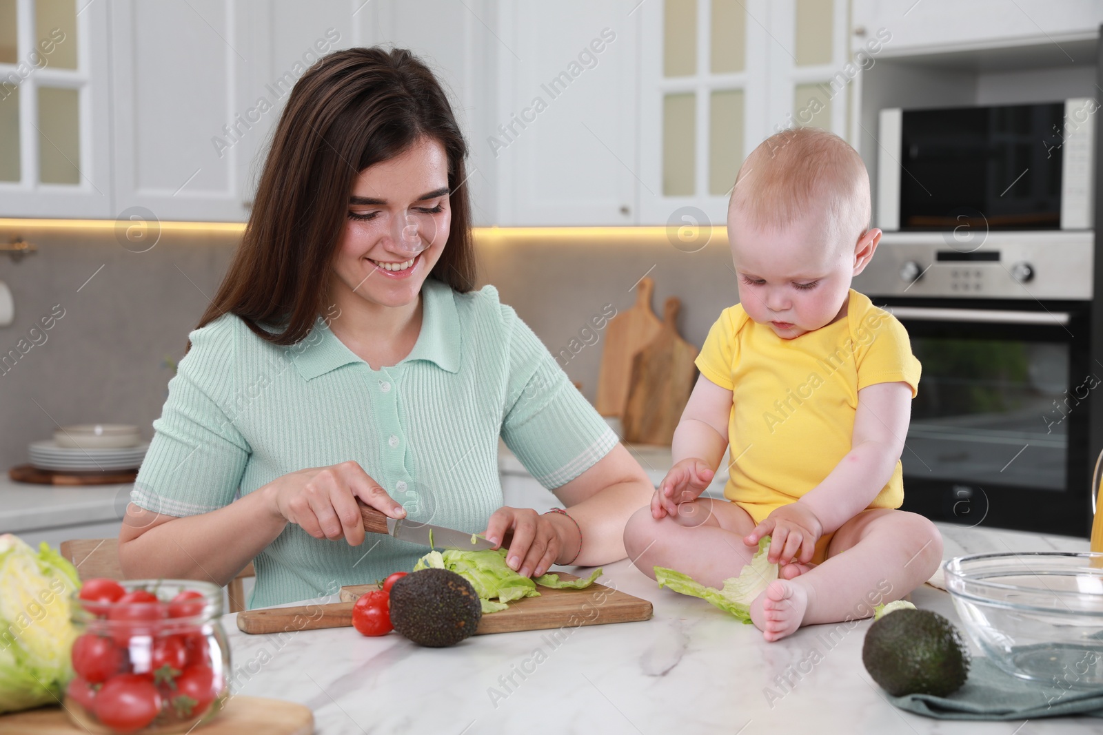 Photo of Happy young woman with her cute baby spending time together in kitchen