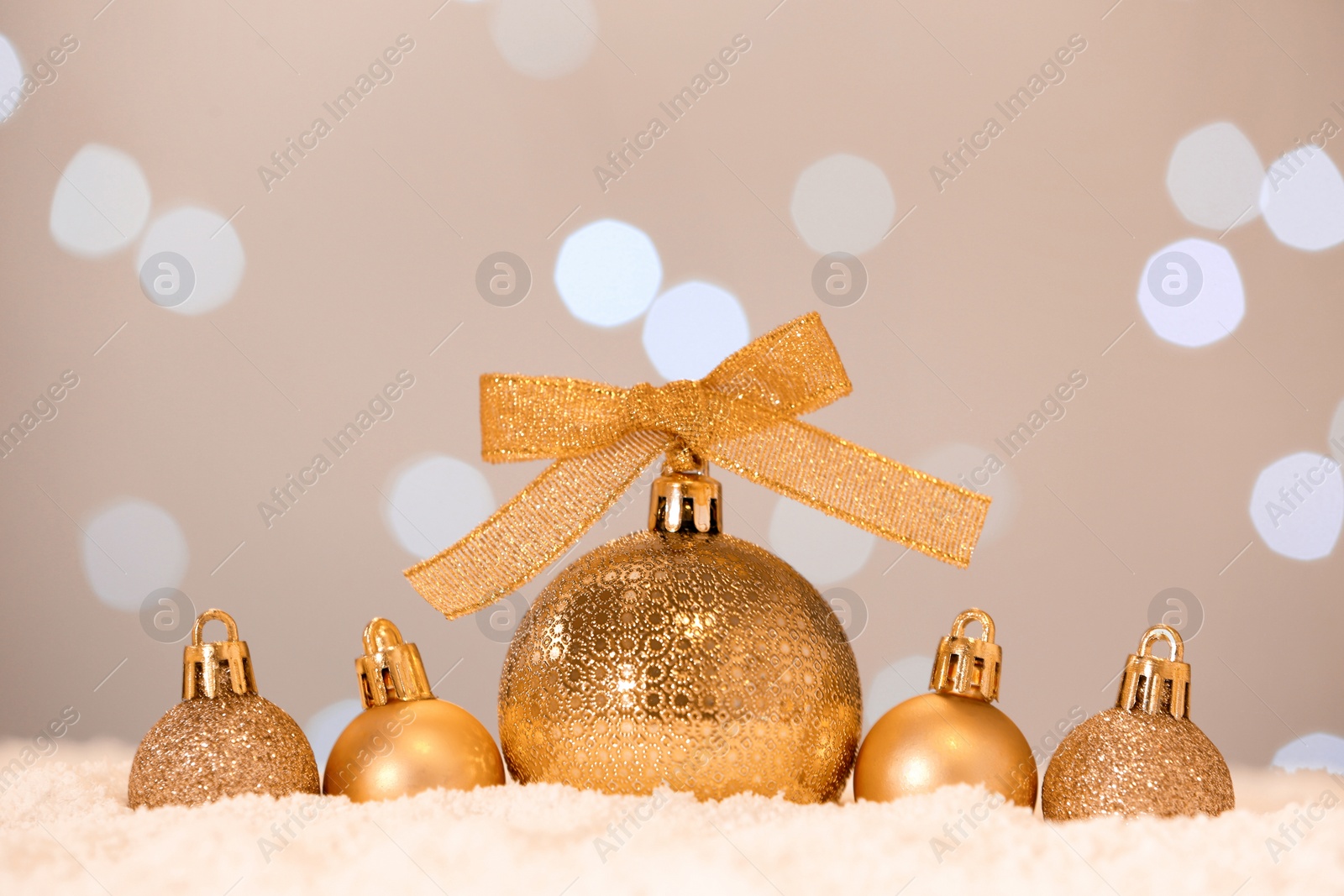 Photo of Beautiful golden Christmas balls on snow against blurred festive lights