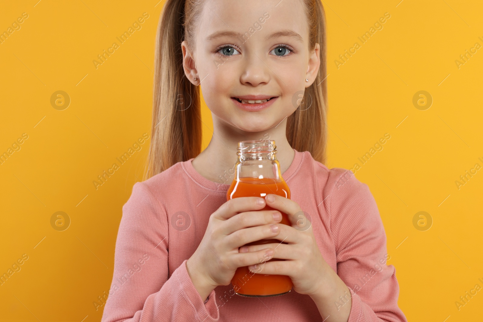 Photo of Cute little girl with glass of fresh juice on orange background