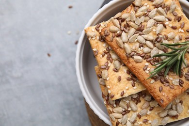 Cereal crackers with flax, sunflower, sesame seeds and rosemary on grey table, top view. Space for text