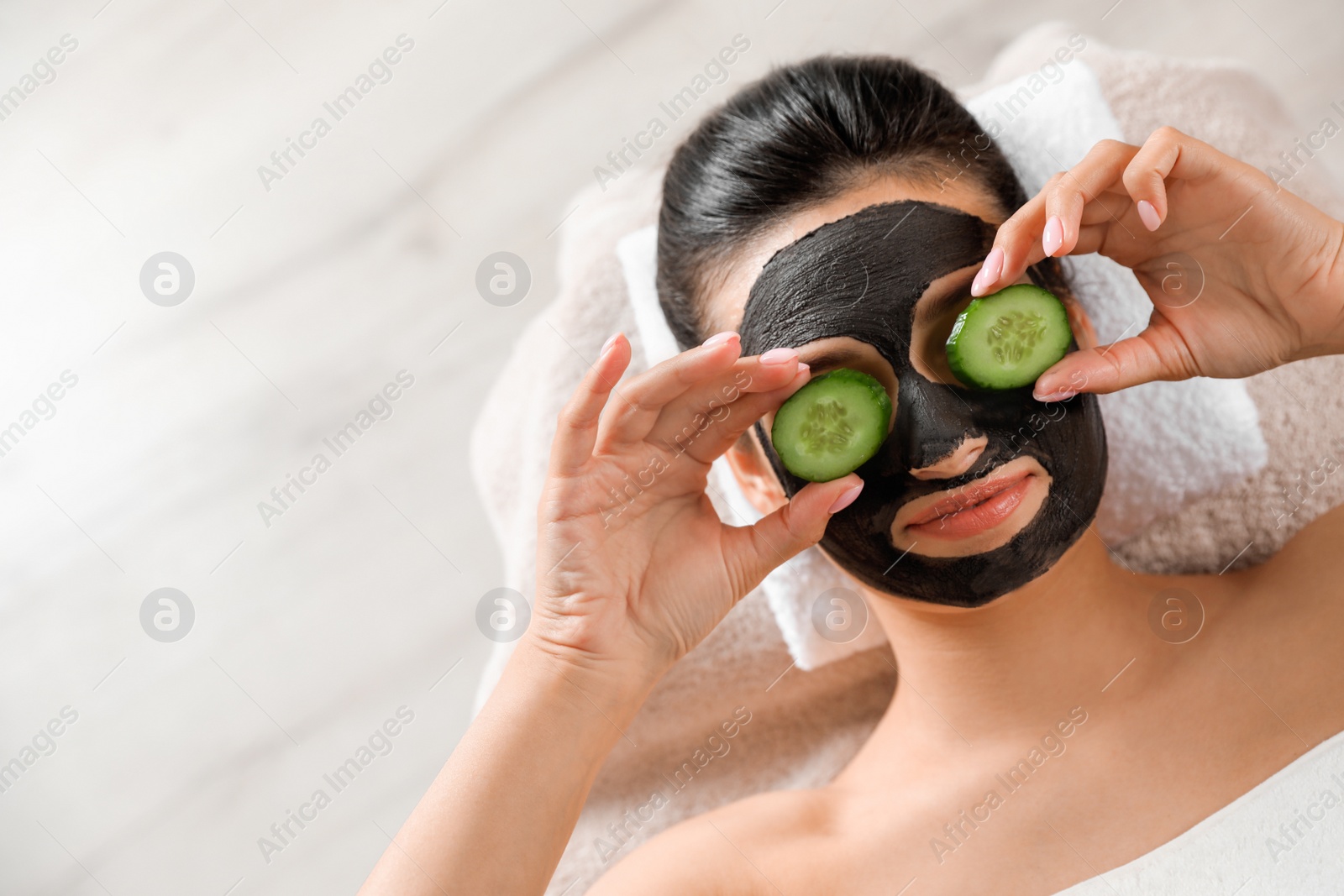 Photo of Beautiful woman with black mask on face and cucumber slices relaxing in spa salon, top view. Space for text