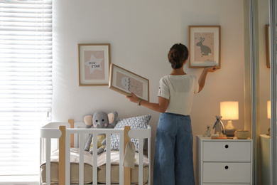 Photo of Decorator hanging pictures on wall in baby room. Interior design