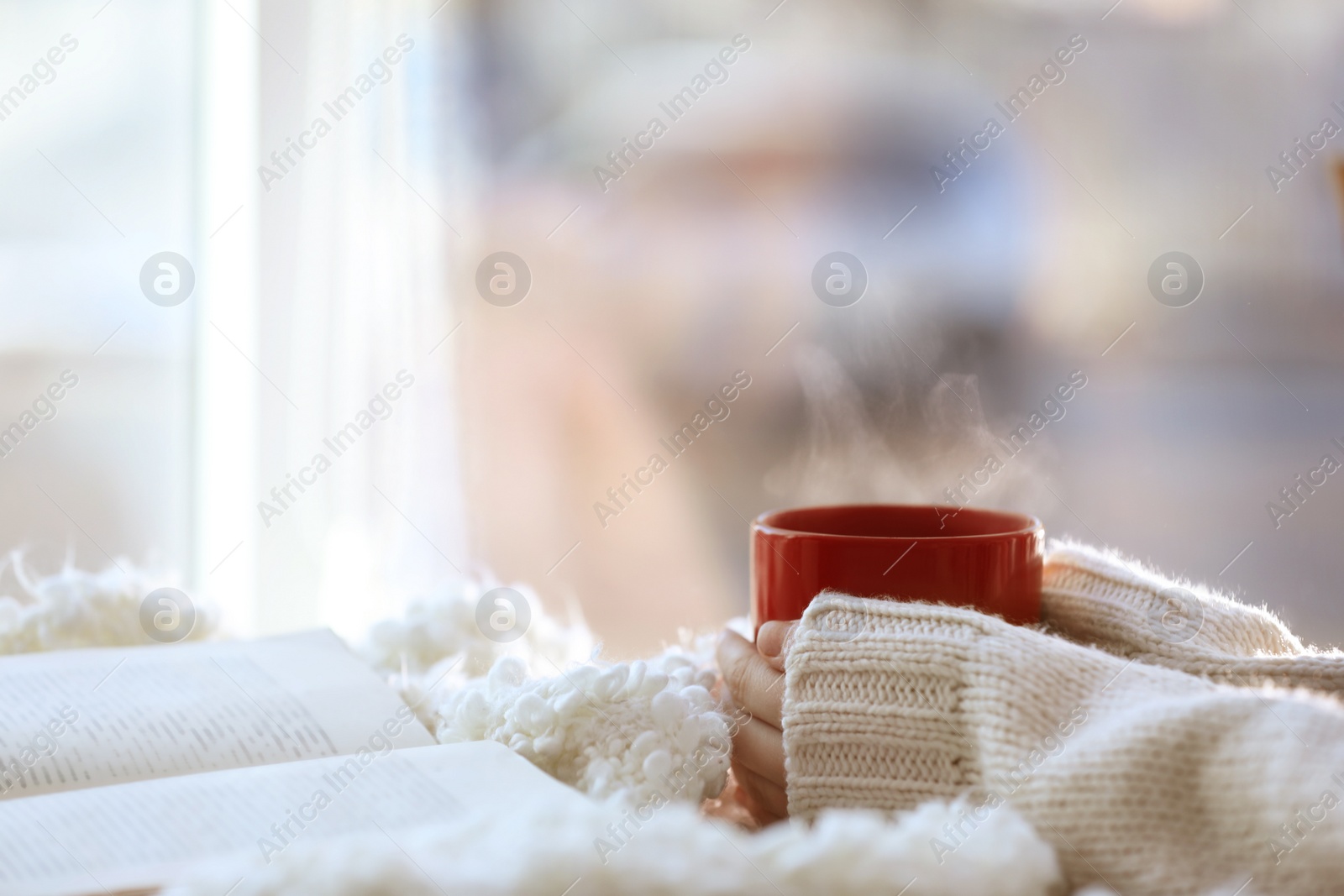 Photo of Woman with cup of coffee and book near window in morning, closeup. Space for text