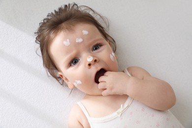 Cute little baby with cream on face in comfortable crib, top view