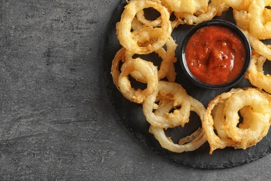Photo of Top view of delicious onion rings and sauce on gray background, closeup. Space for text
