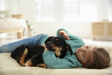 Photo of Little girl with cute puppy lying on soft pillow at home