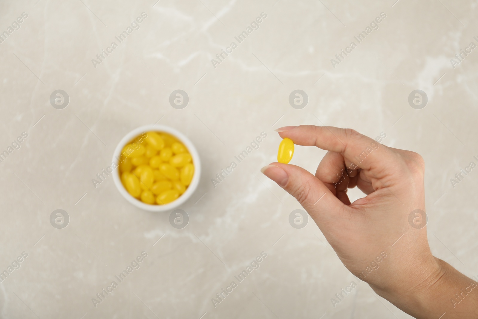 Photo of Woman holding tasty lemon drop above light table, top view