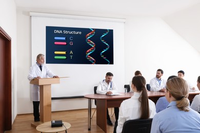 Image of Lecture in biochemistry. Senior speaker near projection screen with illustration. Professors and audience in conference room