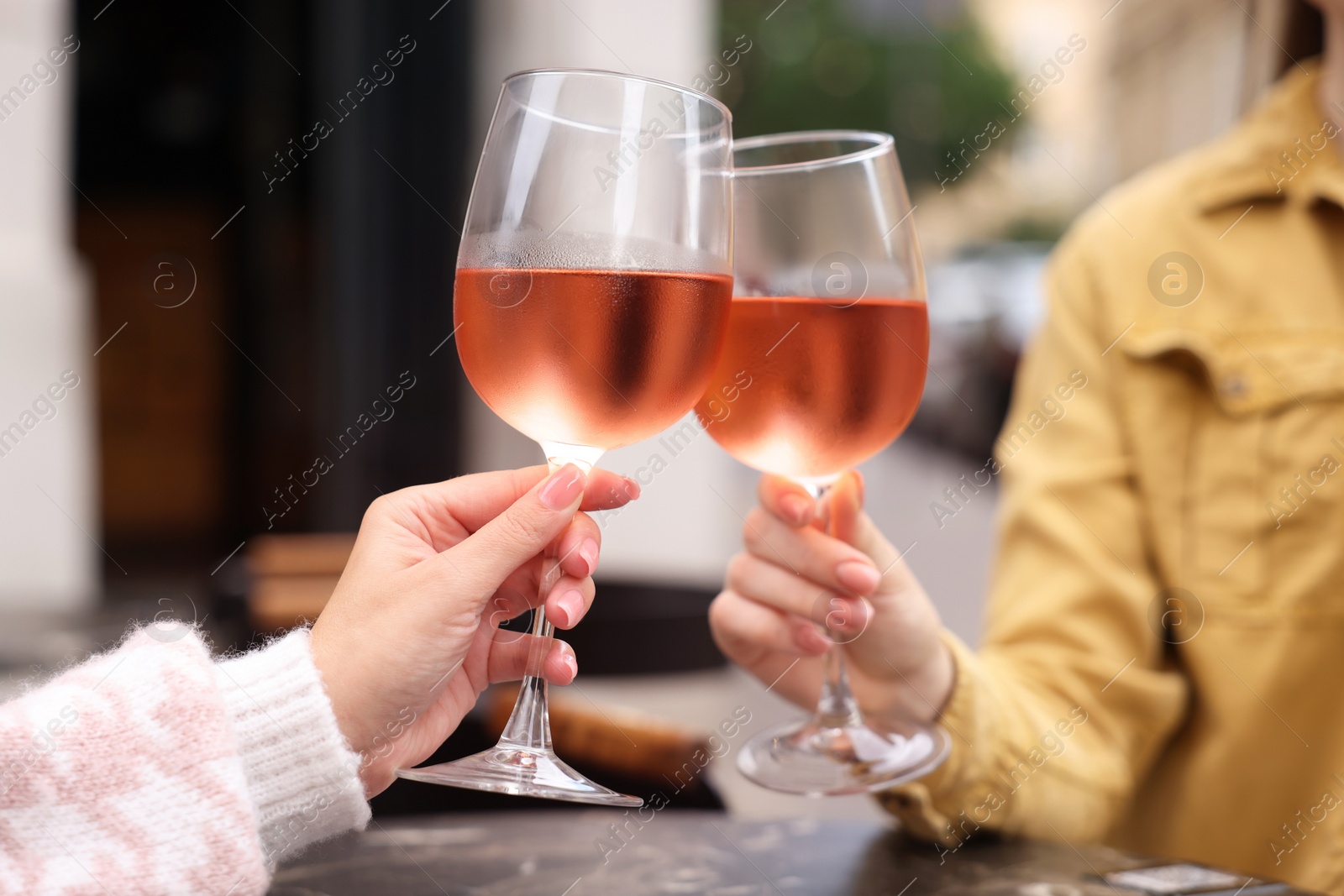 Photo of Women clinking glasses with rose wine at dark marble table in outdoor cafe, closeup
