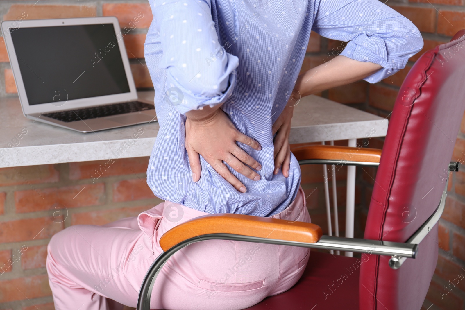 Photo of Woman with lower back pain sitting in office chair at table, closeup