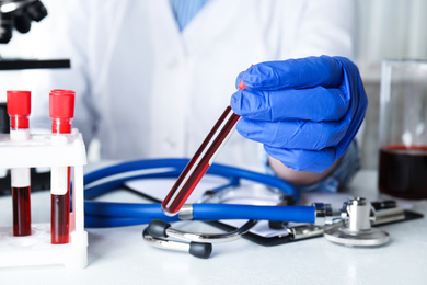 Scientist holding test tube with blood sample at table, closeup. Virus research