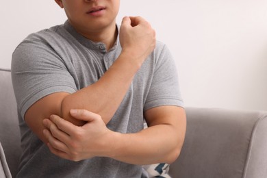 Photo of Man suffering from pain in his elbow on armchair indoors, closeup