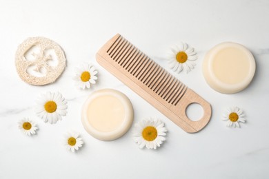 Photo of Solid shampoo bars, comb and chamomiles on white marble table, flat lay. Hair care