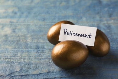 Photo of Golden eggs and card with word Retirement on wooden background, space for text. Pension concept