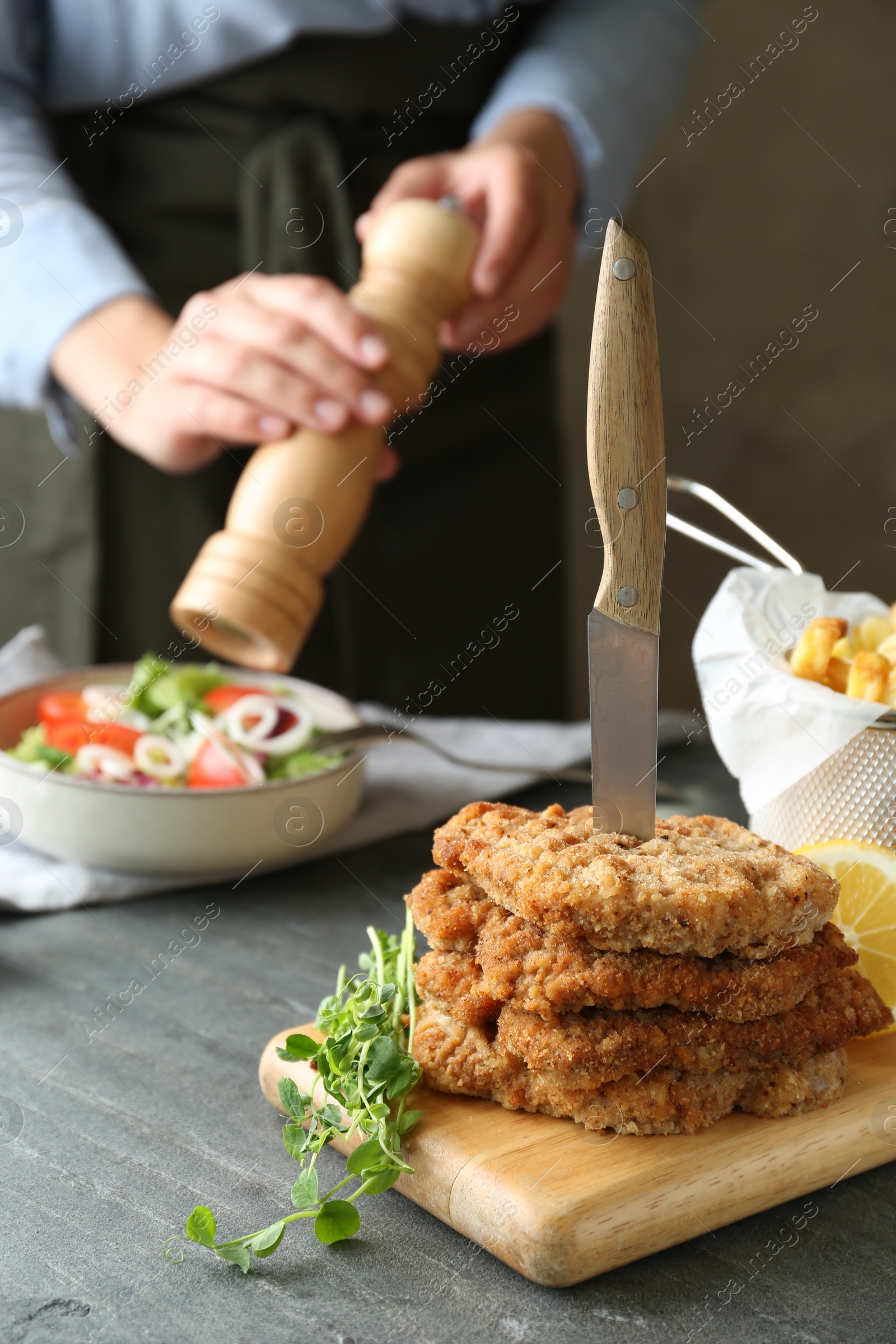 Photo of Tasty schnitzels served with knife and woman adding spices to salad at grey table, closeup