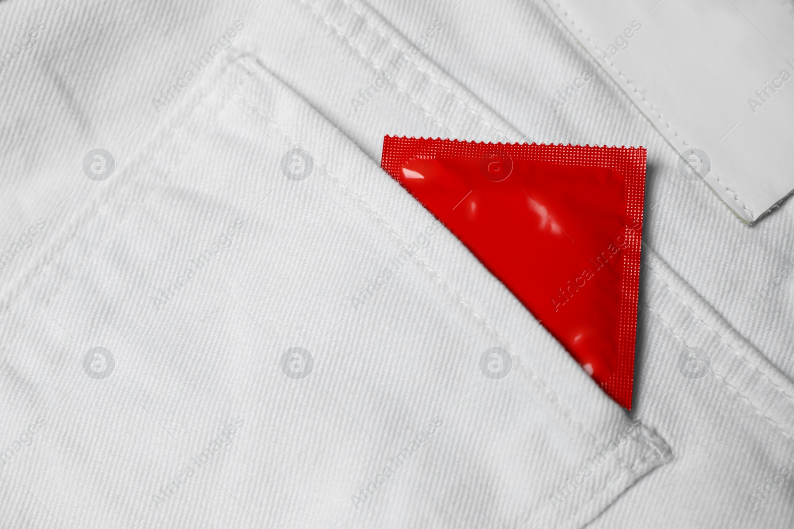 Photo of Packaged condom in white jeans pocket, closeup. Safe sex