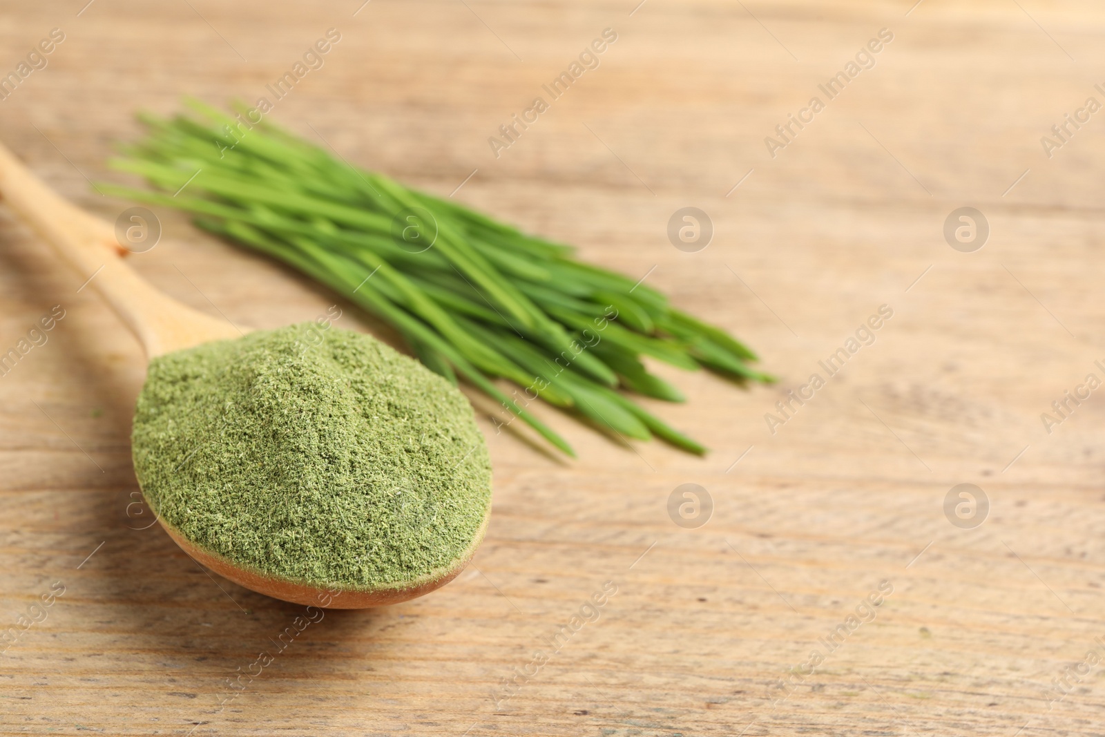 Photo of Wheat grass powder in spoon on wooden table, closeup. Space for text