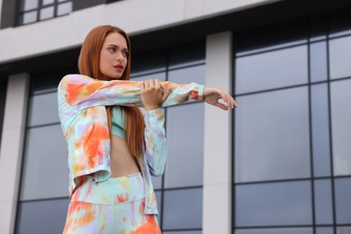 Beautiful woman in stylish gym clothes doing exercises on street, space for text