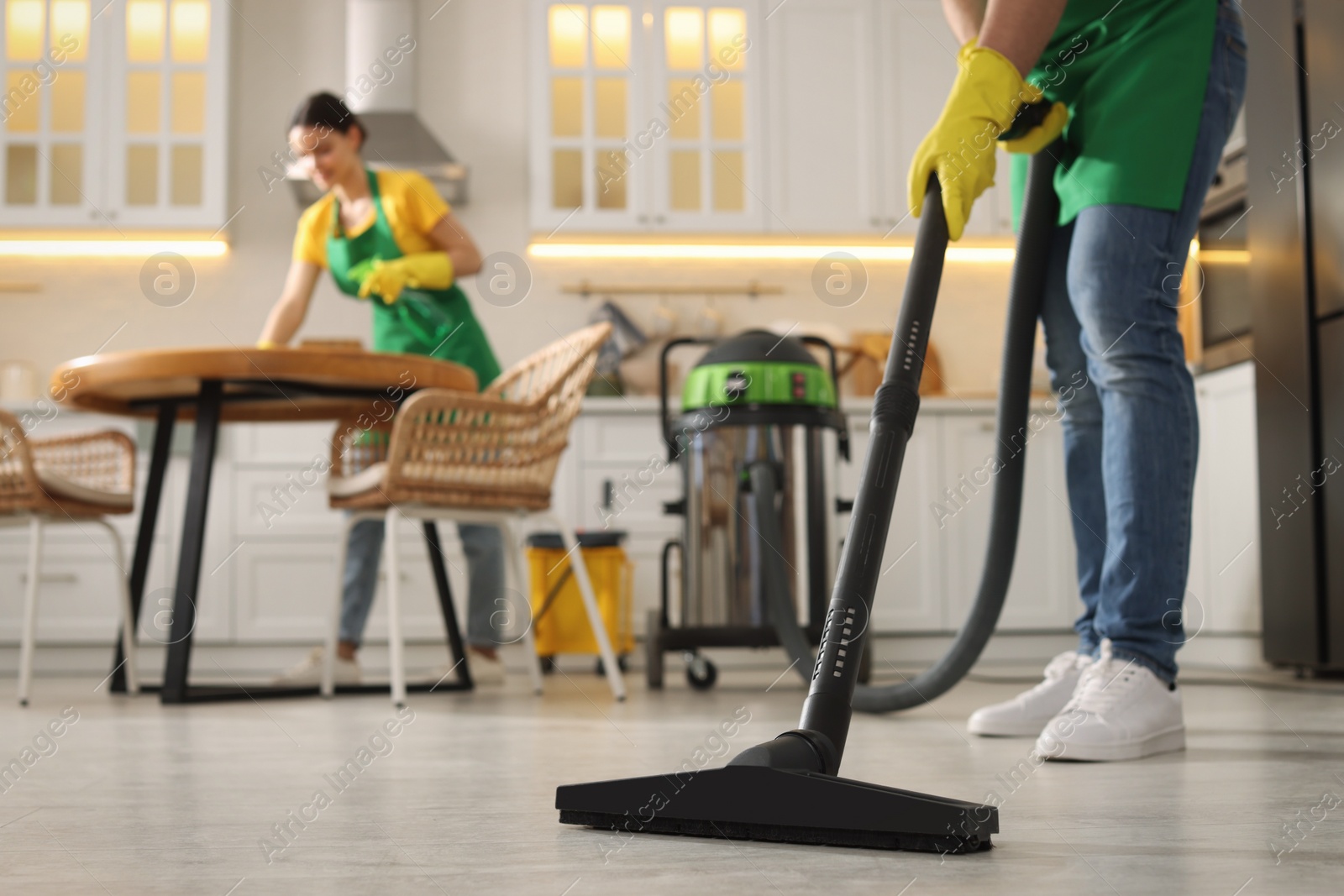 Photo of Professional janitor vacuuming floor in kitchen, closeup. Space for text