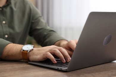 E-learning. Young man using laptop at wooden table indoors, closeup