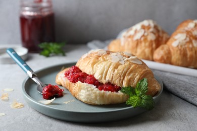 Photo of Delicious croissant with berry jam, almond flakes and spoon on grey table