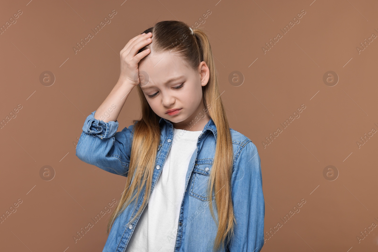 Photo of Little girl suffering from headache on brown background