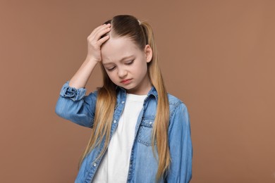 Little girl suffering from headache on brown background