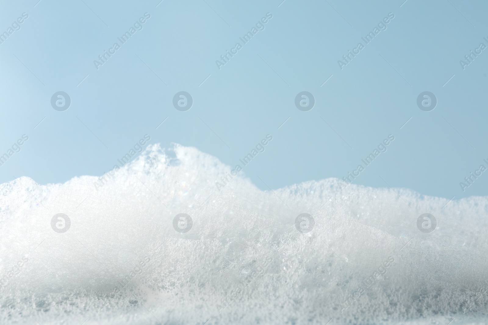 Photo of Fluffy bath foam on light blue background, closeup. Space for text