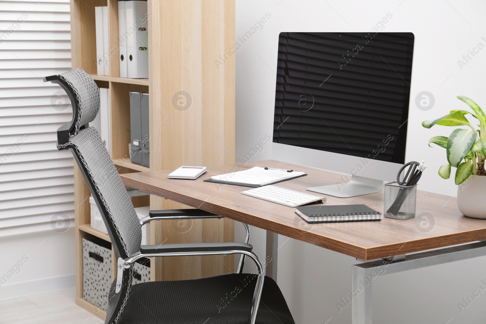 Photo of Cozy workspace with computer on desk, chair and bookcase near white wall at home