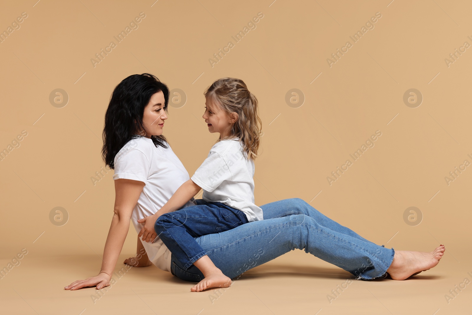 Photo of Beautiful mother with little daughter sitting on beige background