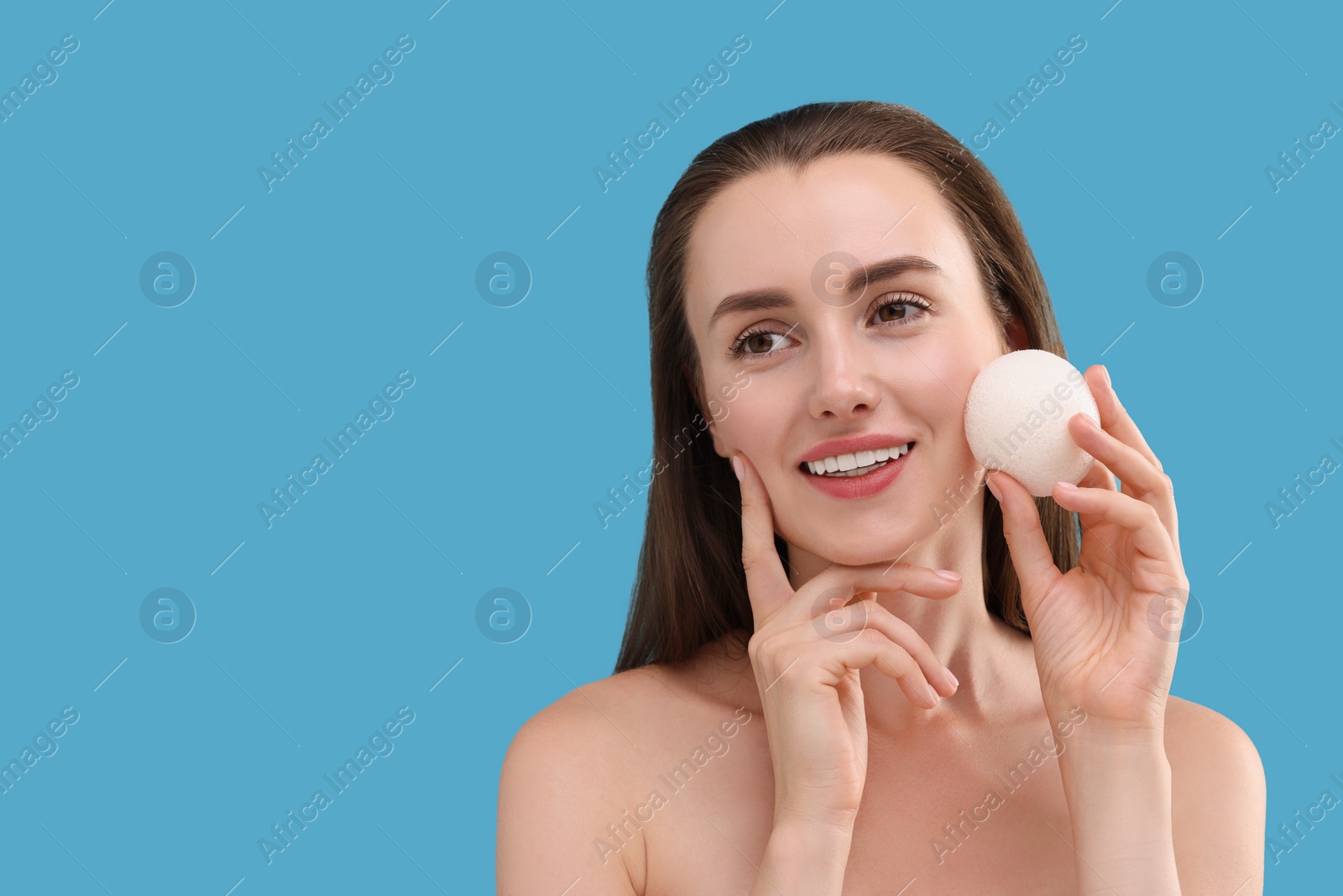 Photo of Happy young woman holding face sponge on light blue background. Space for text