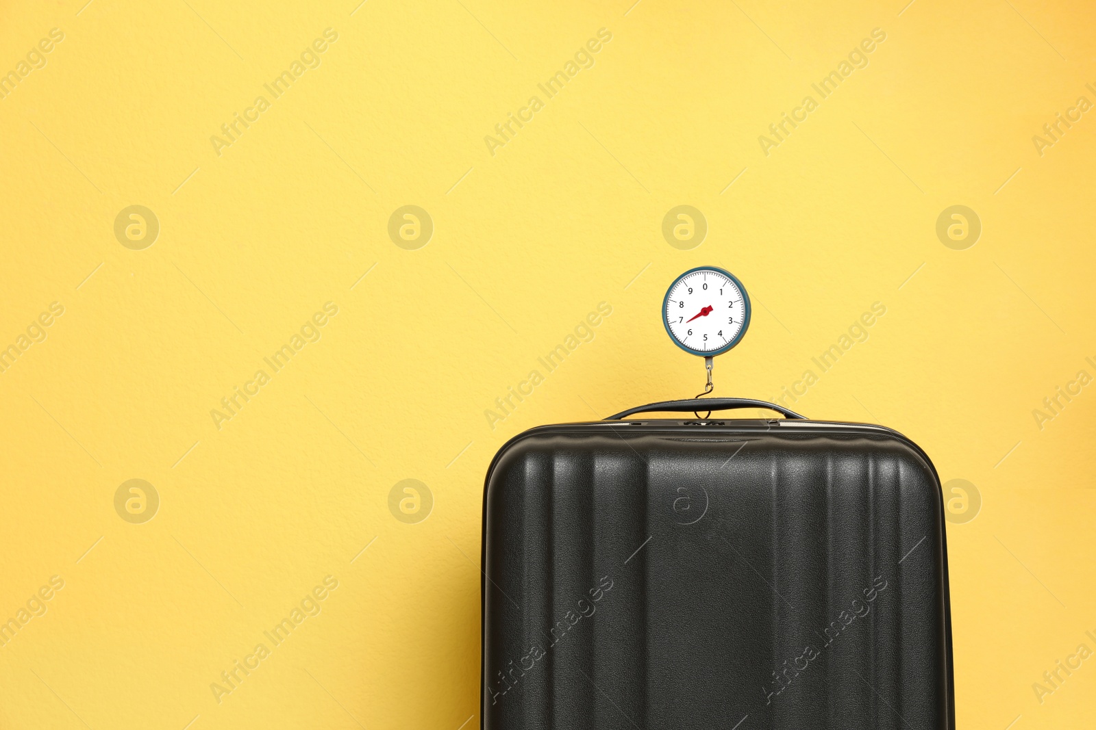 Photo of Modern suitcase and hanging scales against color background, space for text