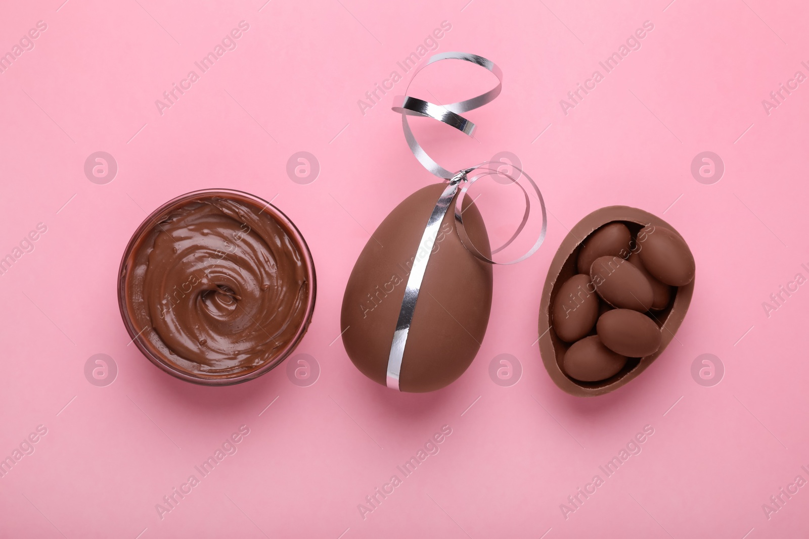 Photo of Delicious chocolate eggs, paste and sweets on pink background, flat lay