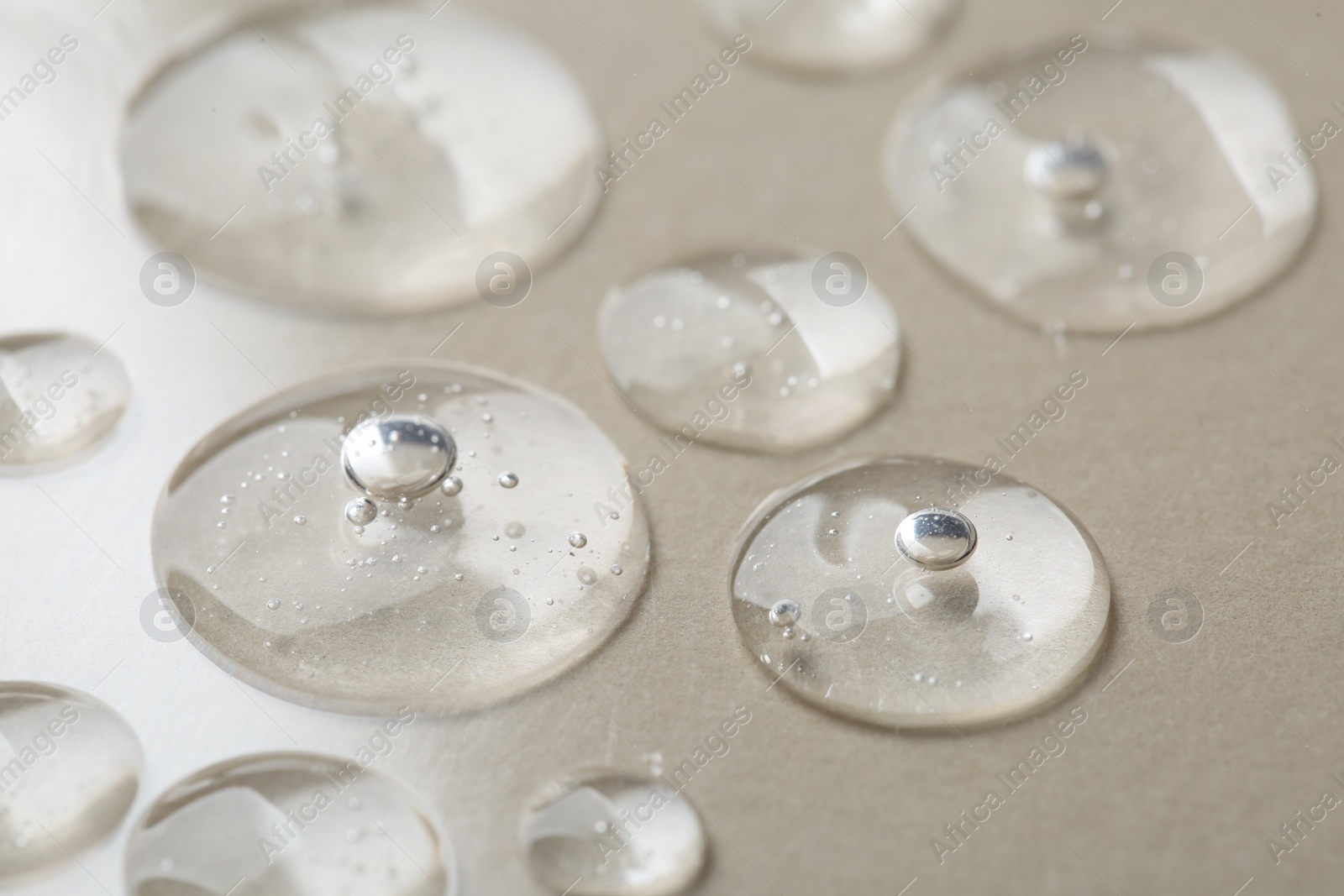 Photo of Drops of cosmetic serum on beige background, macro view