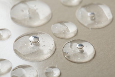 Photo of Drops of cosmetic serum on beige background, macro view